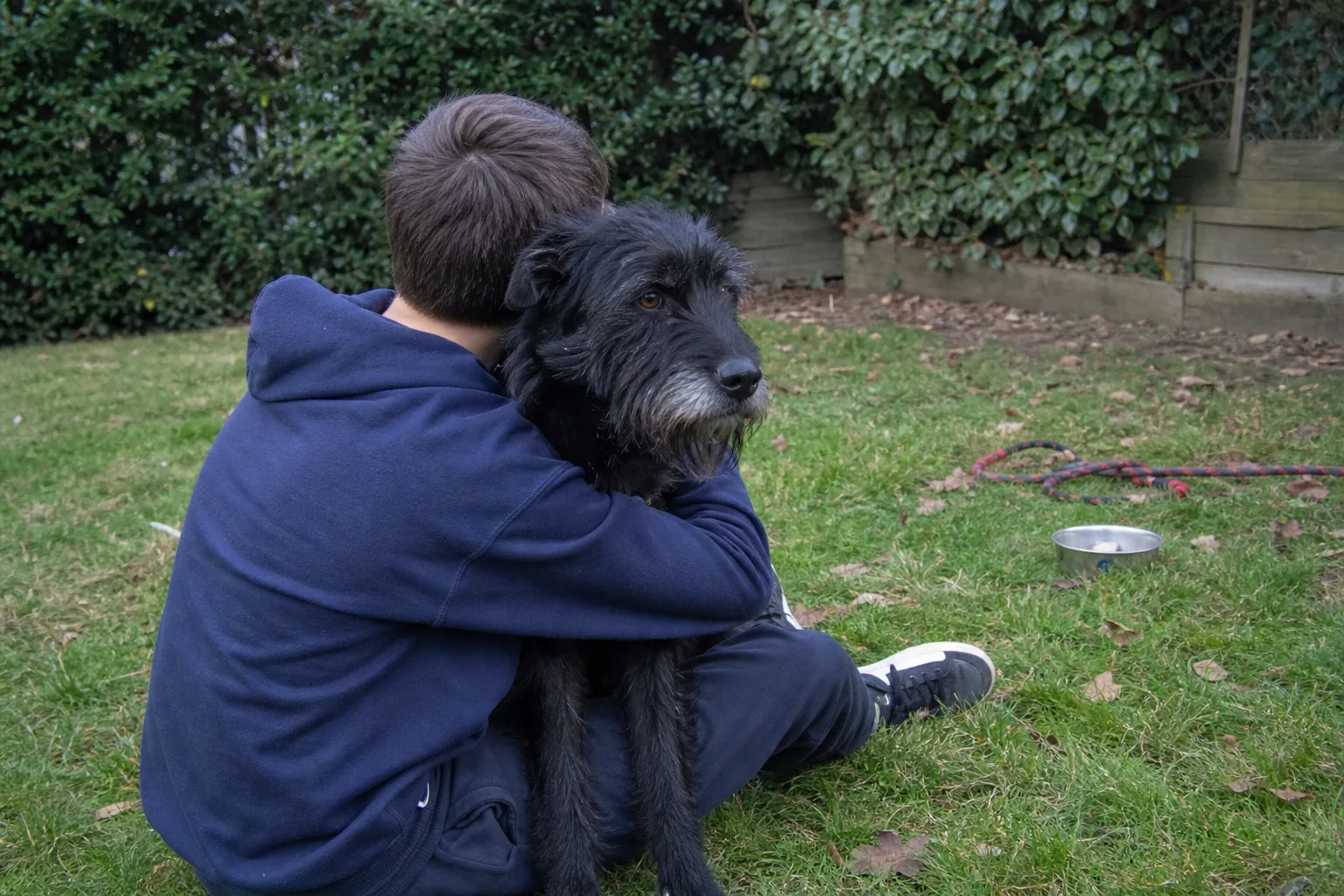 Un adolescent assis dans l'herbe, les bras autour du cou de son chien adopté en refuge