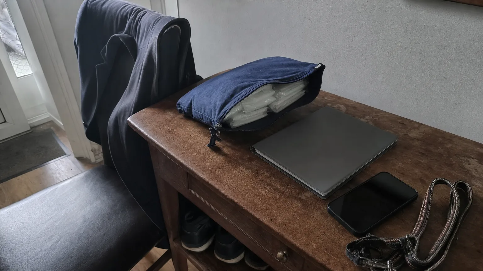 Des compresses emballées et une pochette côtoient un dossier fermé et un téléphone sur une table d’entrée