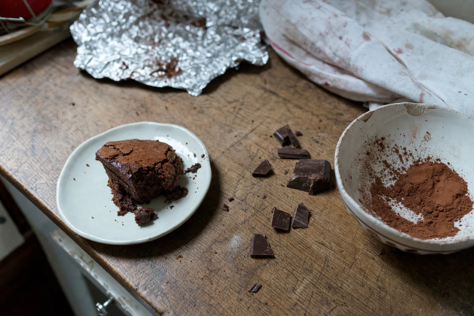 Une part de gâteau et des morceaux de chocolat de tailles différentes restent sur une planche de cuisine marquée par l’usage